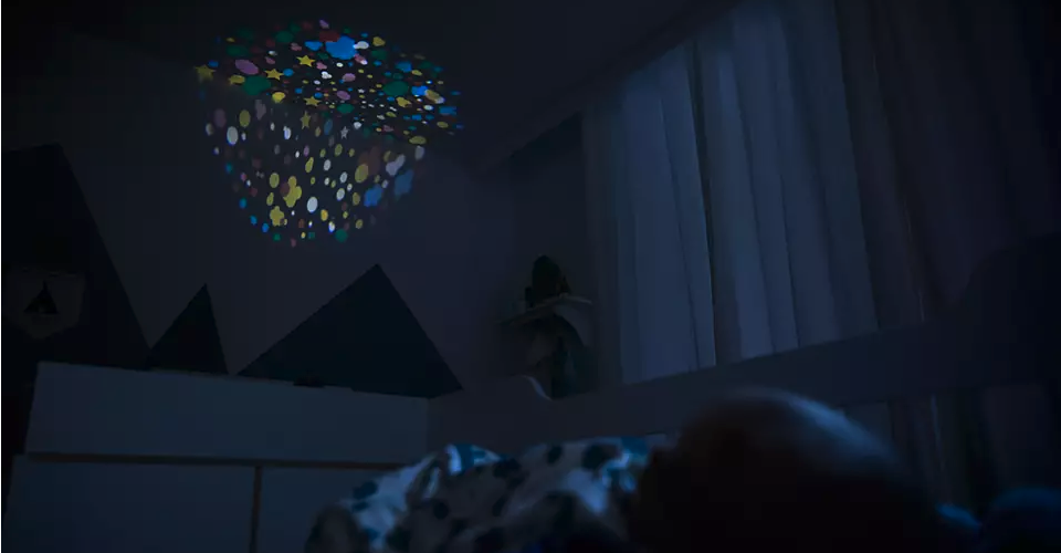 bébé qui dort dans son lit avec projection d'étoiles au plafond